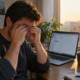Remote worker rubbing tired eyes at a desk in the late afternoon, illustrating digital eye strain